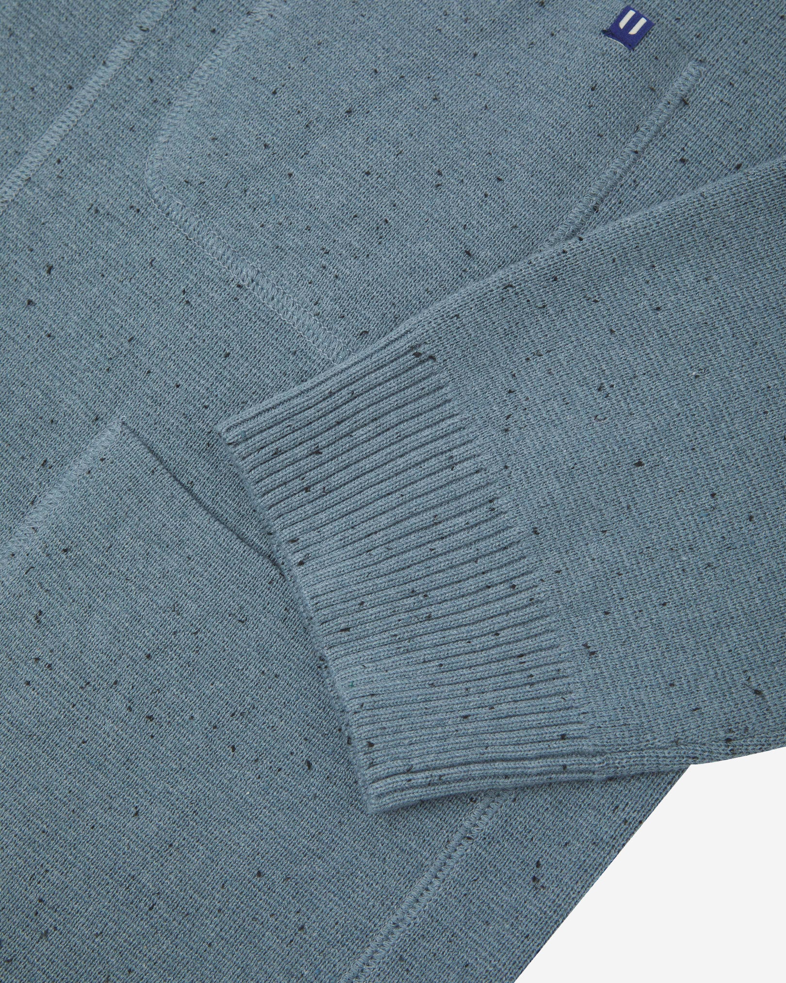 Close-up view of ribbed cuff and pockets of the knitted organic cotton, blue-grey cardigan. Discreet Uskees branding label visible on chest pocket.