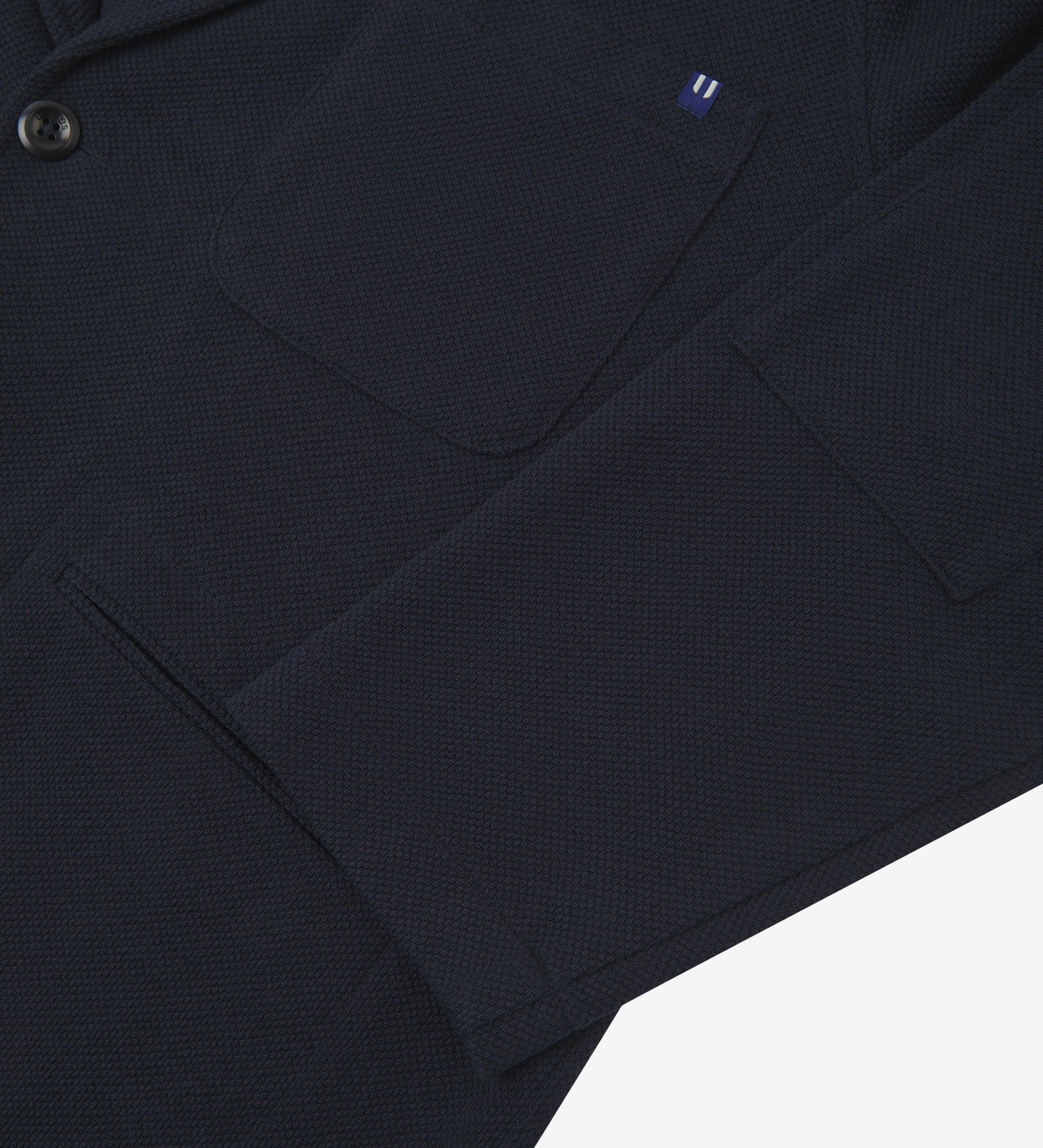 Close-up view of cuff and pockets of knitted organic cotton, midnight blue blazer. Subtle Uskees branding label on the chest patch pocket.