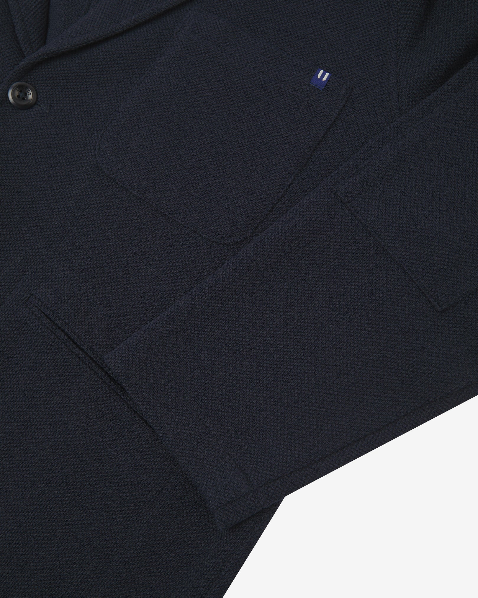 Close-up view of cuff and pockets of knitted organic cotton, midnight blue blazer. Subtle Uskees branding label on the chest patch pocket.