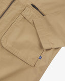 Close-up of an Uskees beige ripstop jacket with a zipped pocket and a brand logo tab on a white background
