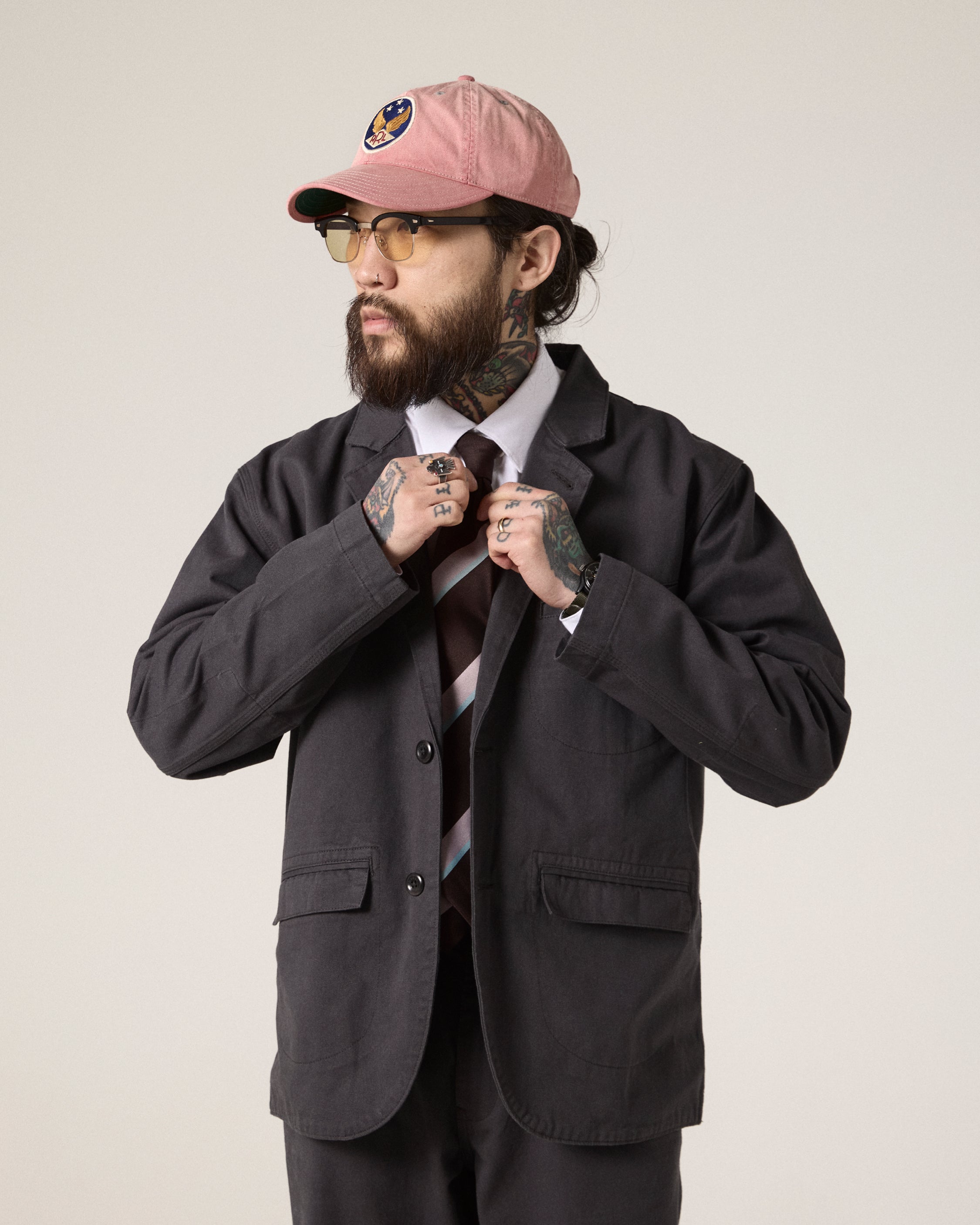 Bearded male model looking to his right wearing the Uskees charcoal docklands blazer, matching trousers and a white shirt. Can see tattoos on his hands.