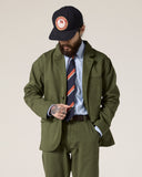 Front view of male model wearing the Uskees green docklands jacket, matching pants, pale blue shirt and striped tie.