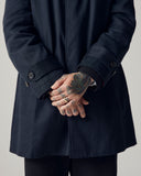 Male model wearing a dark blue Uskees car coat showing his arms and hands with tattoos, on a plain background