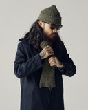 Male model wearing an Uskees dark blue car coat, Uskees green wool hat and matching scarf against a plain background