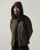 Model wearing Uskees army green Evo shell coat with focus on hood and cargo pockets.