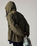 Model wearing Uskees army green Evo shell coat with focus on hood and back vent.