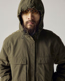 Model wearing Uskees army green Evo shell coat with focus on hood and breast cargo pockets.