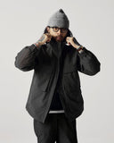 Model wearing Uskees charcoal-grey Evo shell coat with focus on hood and cargo pockets.
