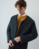 A man wearing an Uskee dark charcoal zip-up liner jacket over a mustard yellow knit sweater and a white collared shirt, standing against a light gray studio background.