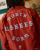 Close-up back view of a man wearing a clay red Uskees jacket with focus on the the North Born Uskees slogan.