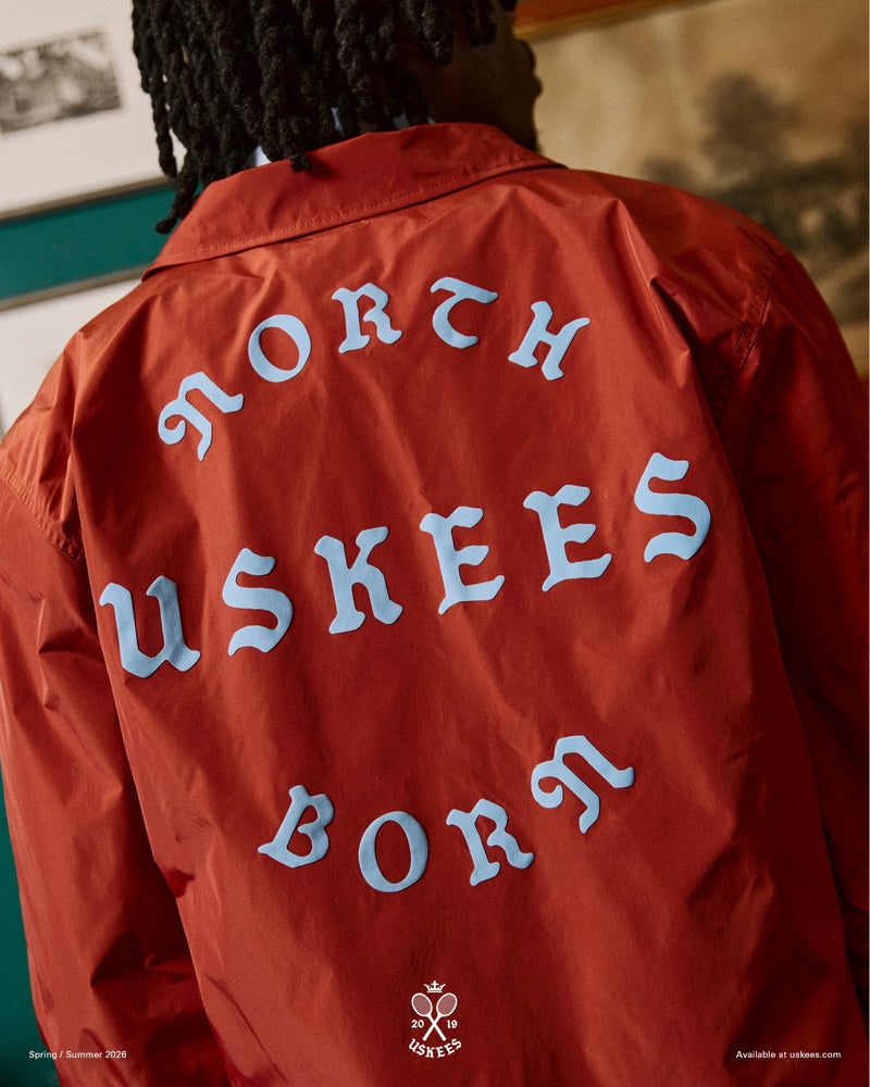 Close-up back view of a man wearing a clay red Uskees jacket with focus on the the North Born Uskees slogan.