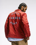 Top-half back view modelling Uskees 3052 clay red blue coach jacket with focus on the the North Born Uskees slogan in blue.