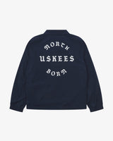 Back view flat shot of Uskees navy blue coach jacket for men with focus on the the North Born Uskees slogan, straight-cut hem and elasticated cuffs.