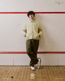Full-length front view of a man wearing a yellow checkered Uskees jacket with hands in side pockets. Paired with Uskees green pants.