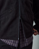 Close-up of an Uskees black zip-front jacket worn over a purple and gray plaid shirt, showing the double-ended zip.