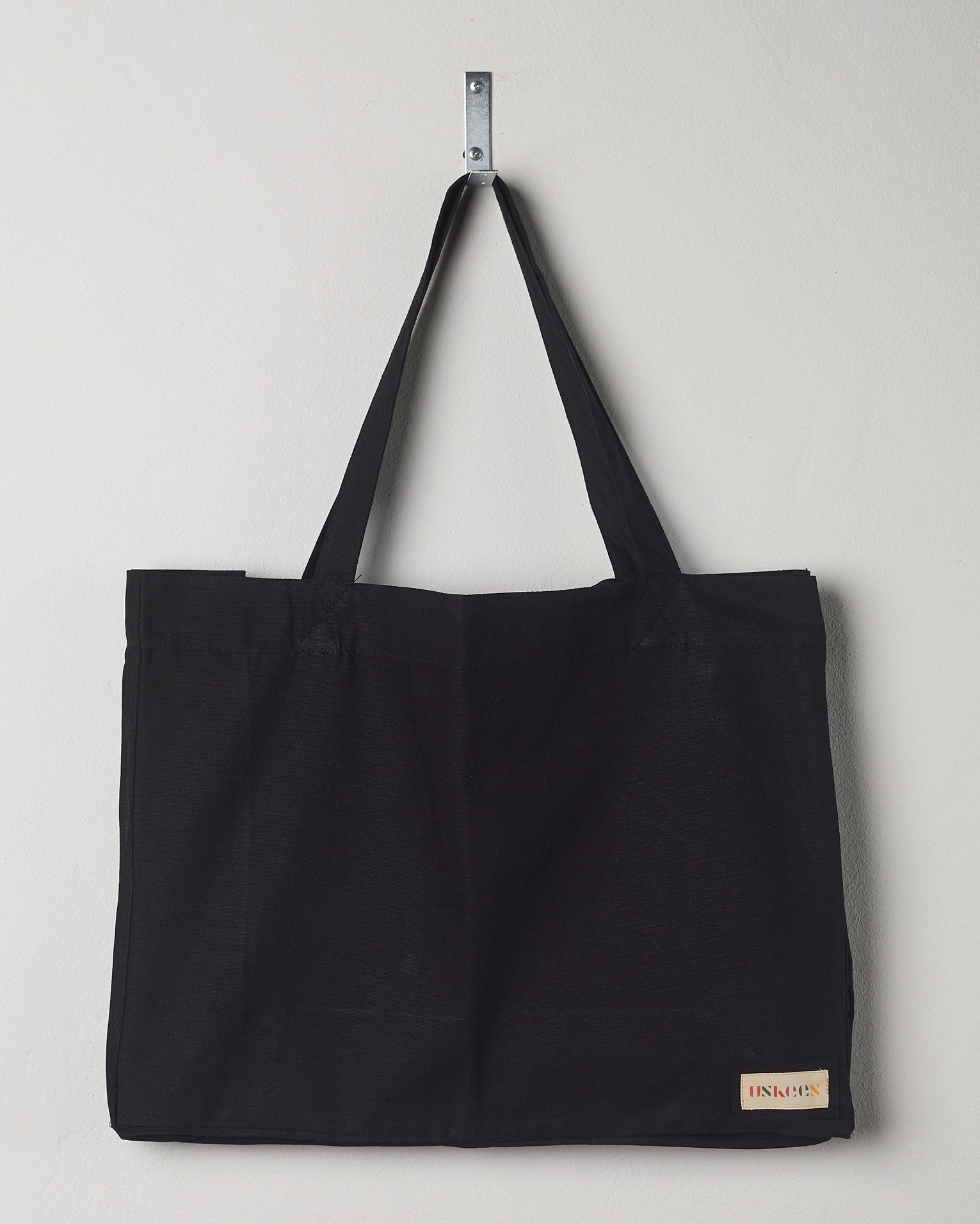 Full front hanging shot of Uskees #4001, large black tote bag, showing double handles and Uskees woven logo. 