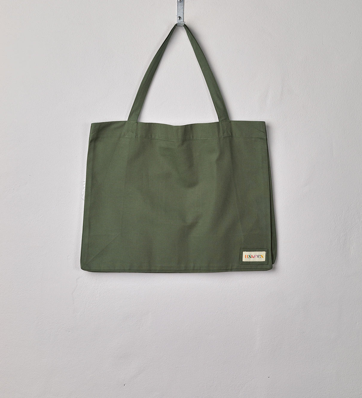 Full front hanging shot of Uskees #4001 large coriander-green tote bag, showing double handles and Uskees woven logo.