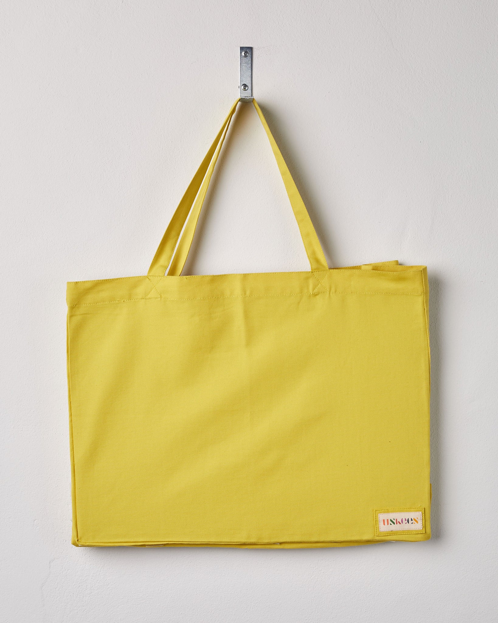 Full, flat view of Uskees #4001, large grapefruit-yellow tote bag, showing twin handles and Uskees woven logo. 