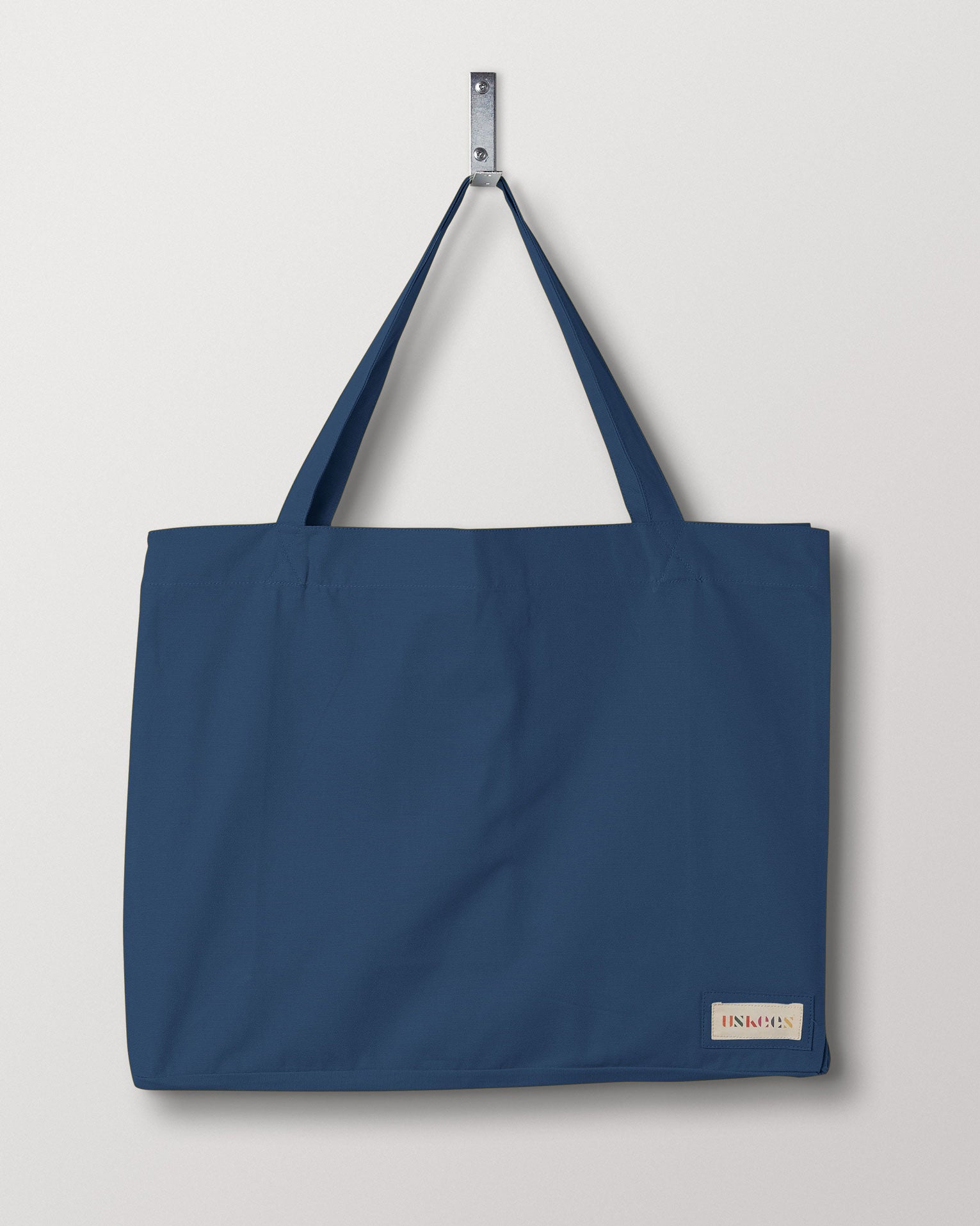 Full front hanging shot of Uskees #4001 large peacock-blue tote bag, showing double handles and Uskees woven logo.