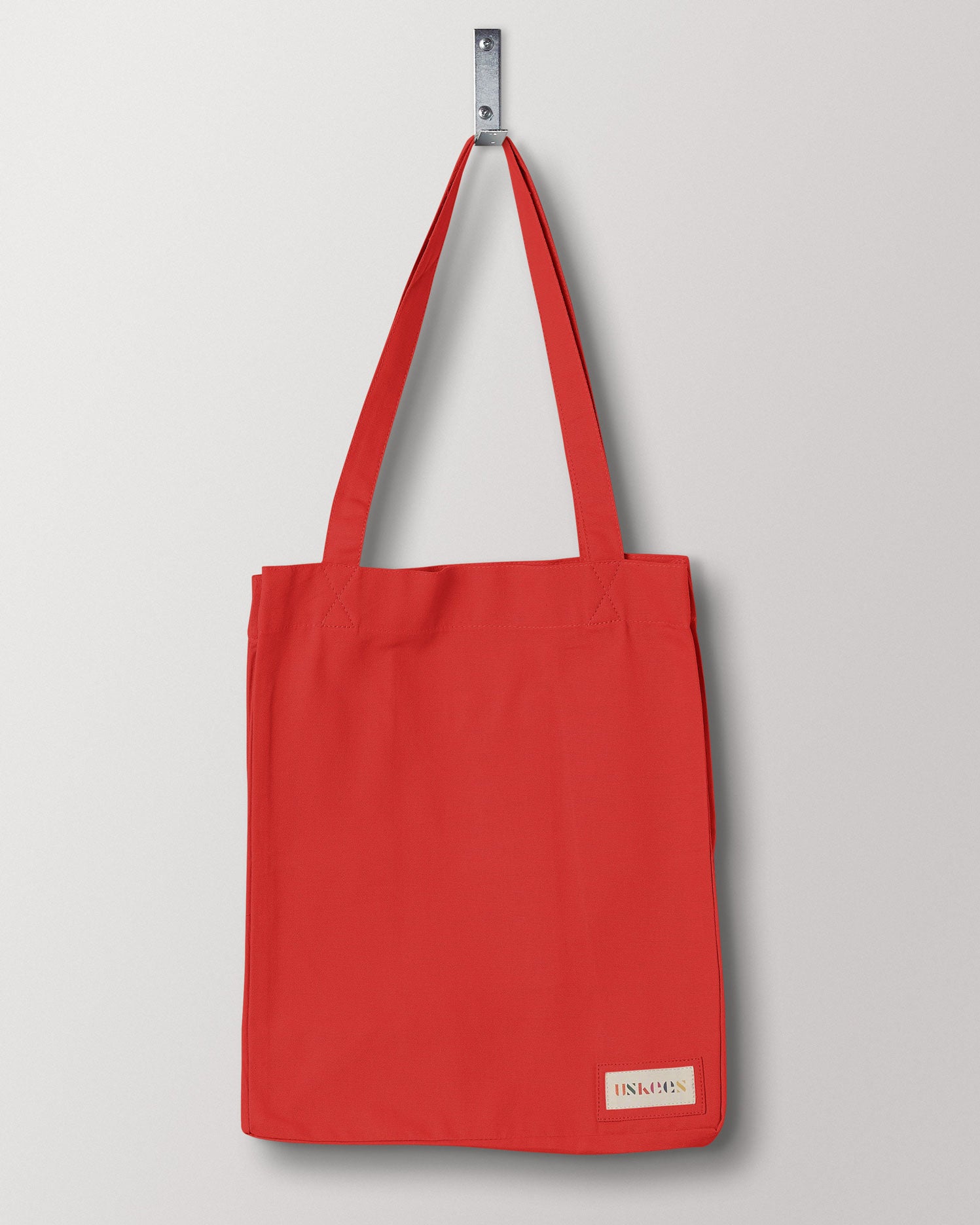Full front hanging shot of Uskees #4002, small bright red tote bag, showing double handles and Uskees woven logo.