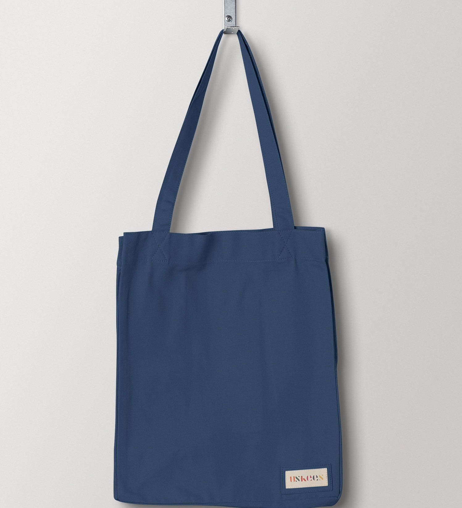 Full front hanging shot of Uskees #4002 small peacock-blue tote bag, showing double handles and Uskees woven logo.