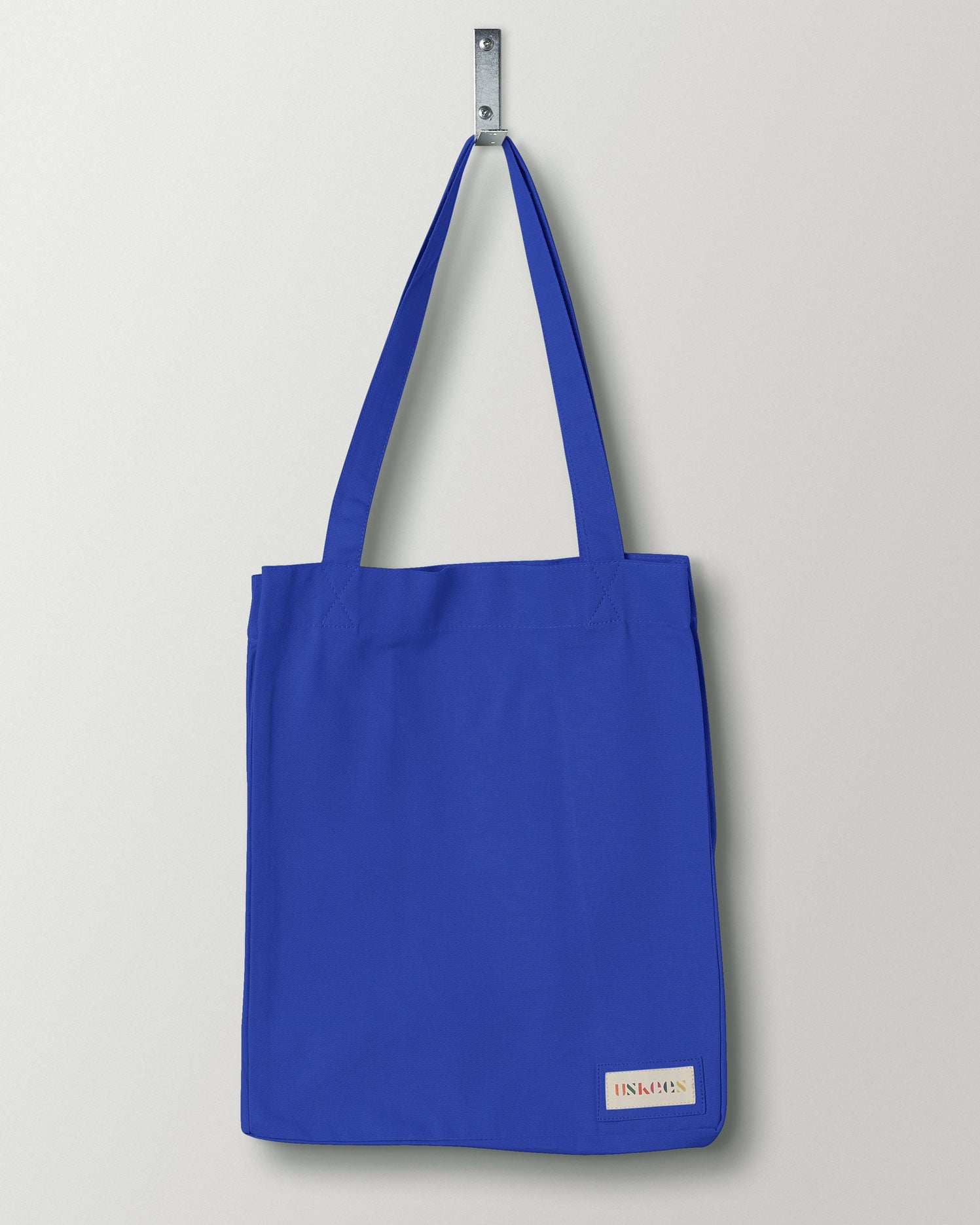 Full front hanging shot of Uskees #4002 small ultra-blue tote bag, showing double handles and Uskees woven logo.