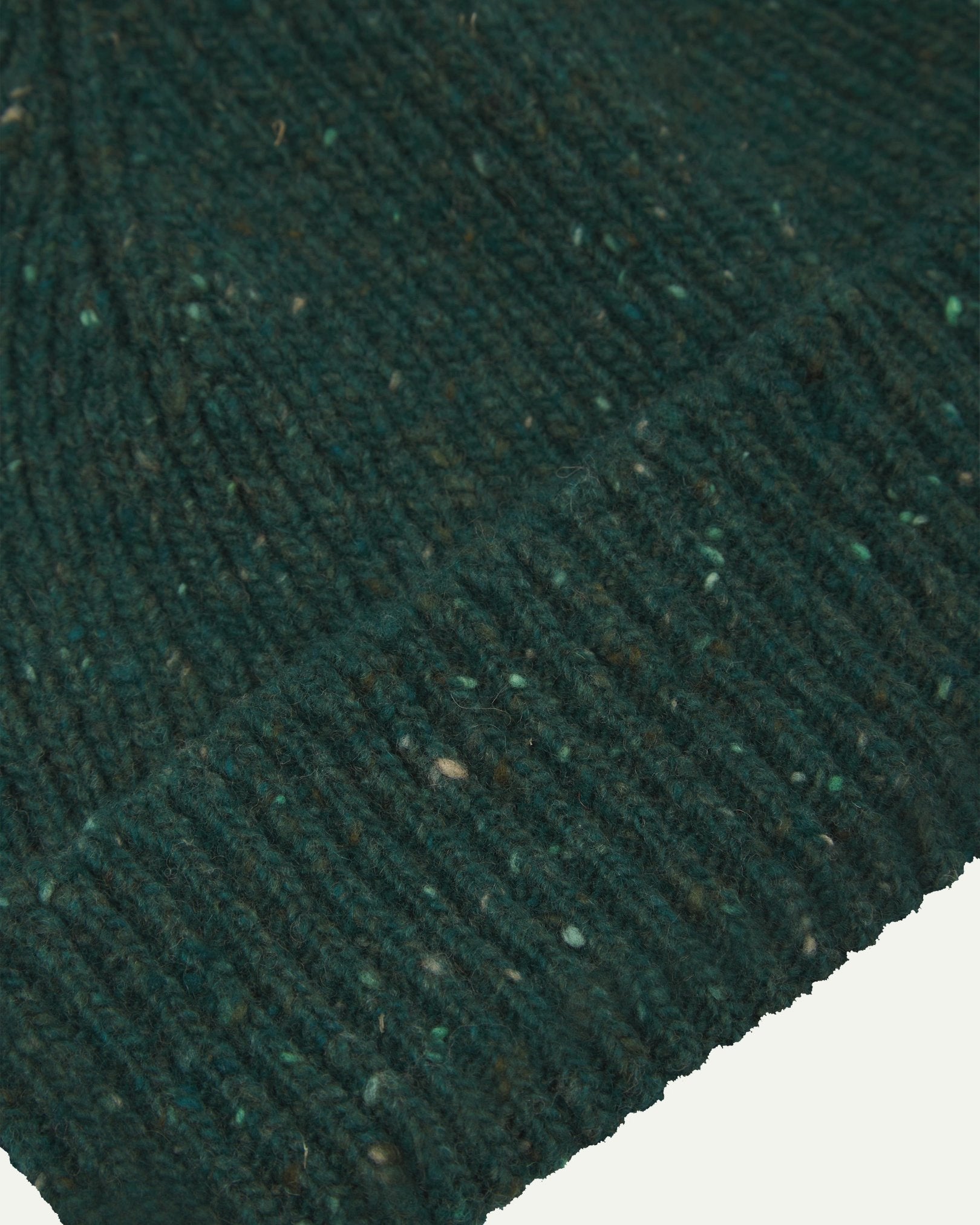 Close-up of the 'mallard green' donegal wool hat from Uskeed, clearly showing the ribbing and multicoloured 'speckled' detail and texture of the natural Scottish merino wool.