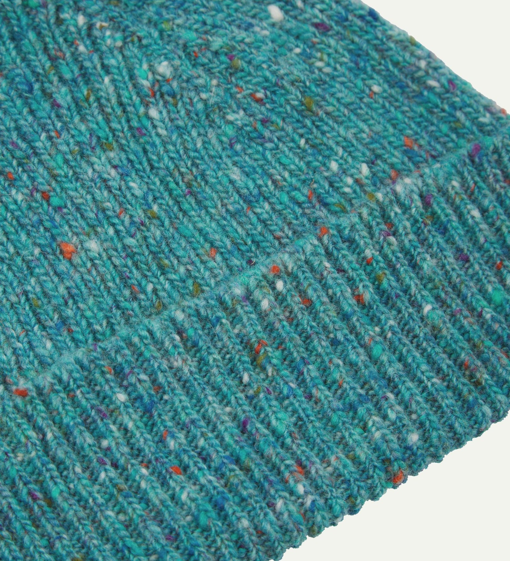 Close-up of the 'ocean green' donegal wool hat from Uskees, clearly showing the ribbing and multicoloured 'speckled' detail and texture of the natural Scottish merino wool.