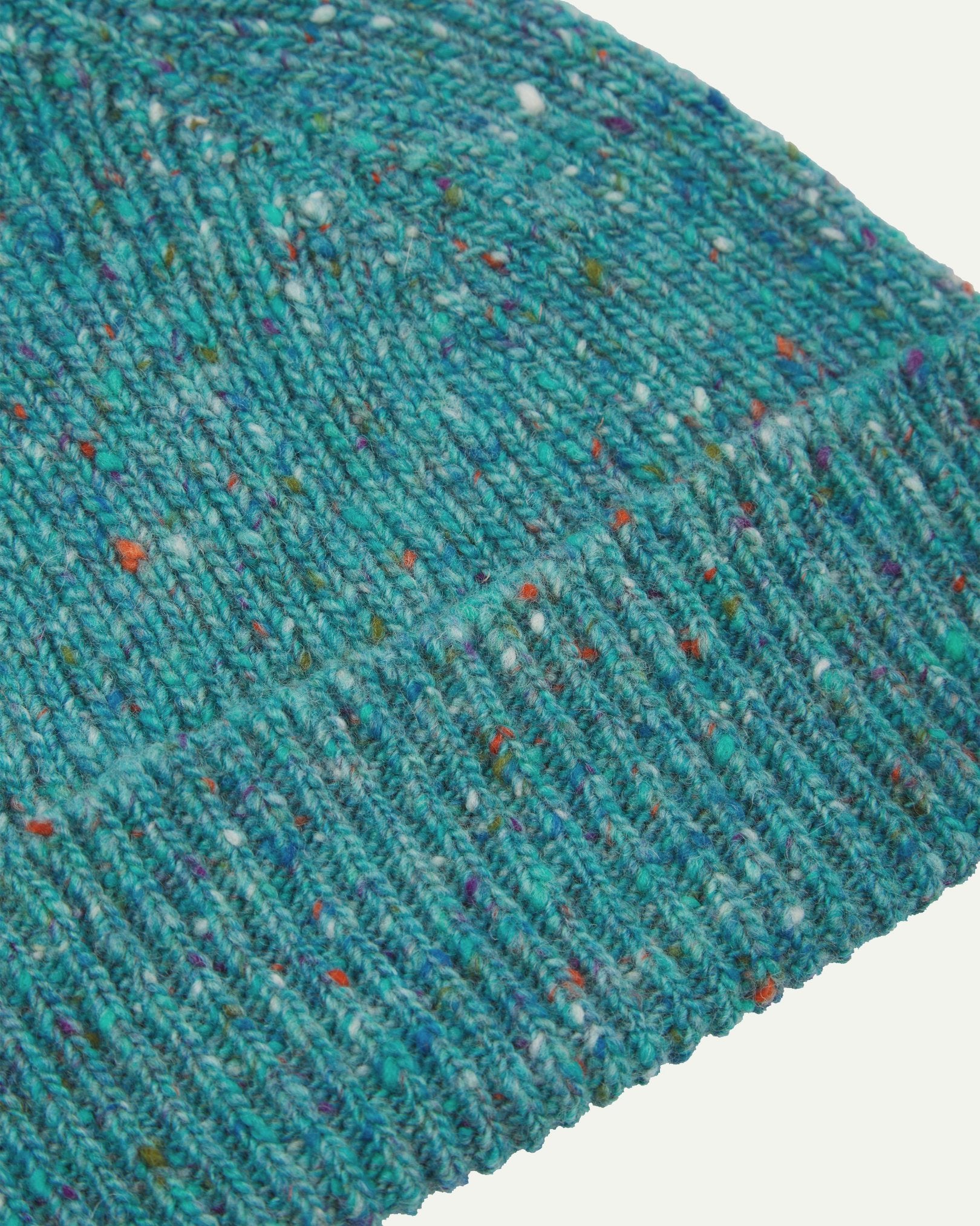 Close-up of the 'ocean green' donegal wool hat from Uskeed, clearly showing the ribbing and multicoloured 'speckled' detail and texture of the natural Scottish merino wool.