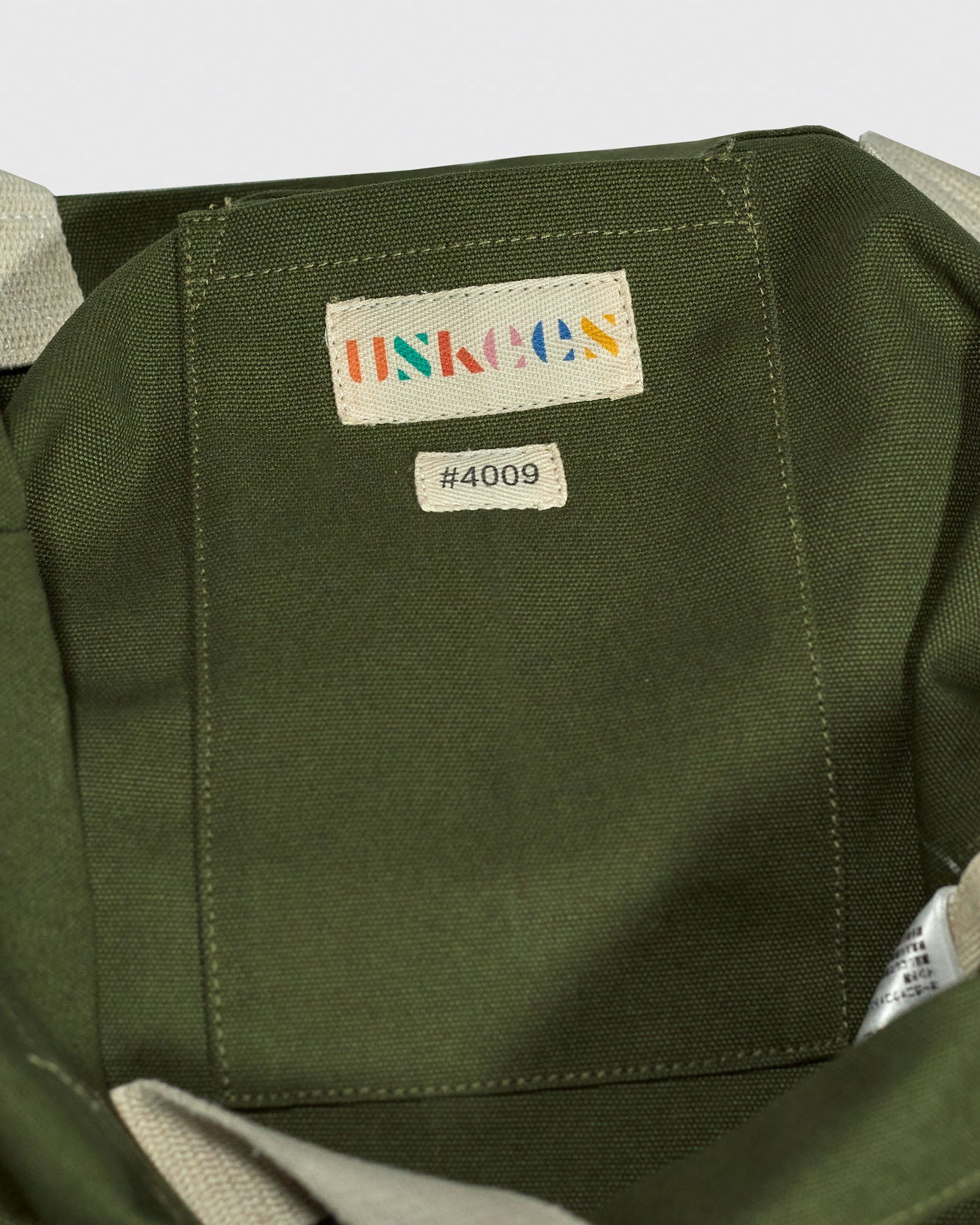 Close-up inside view of Uskees #4009 canvas tote bag in coriander-green with focus on the internal patch pocket and branding logo.