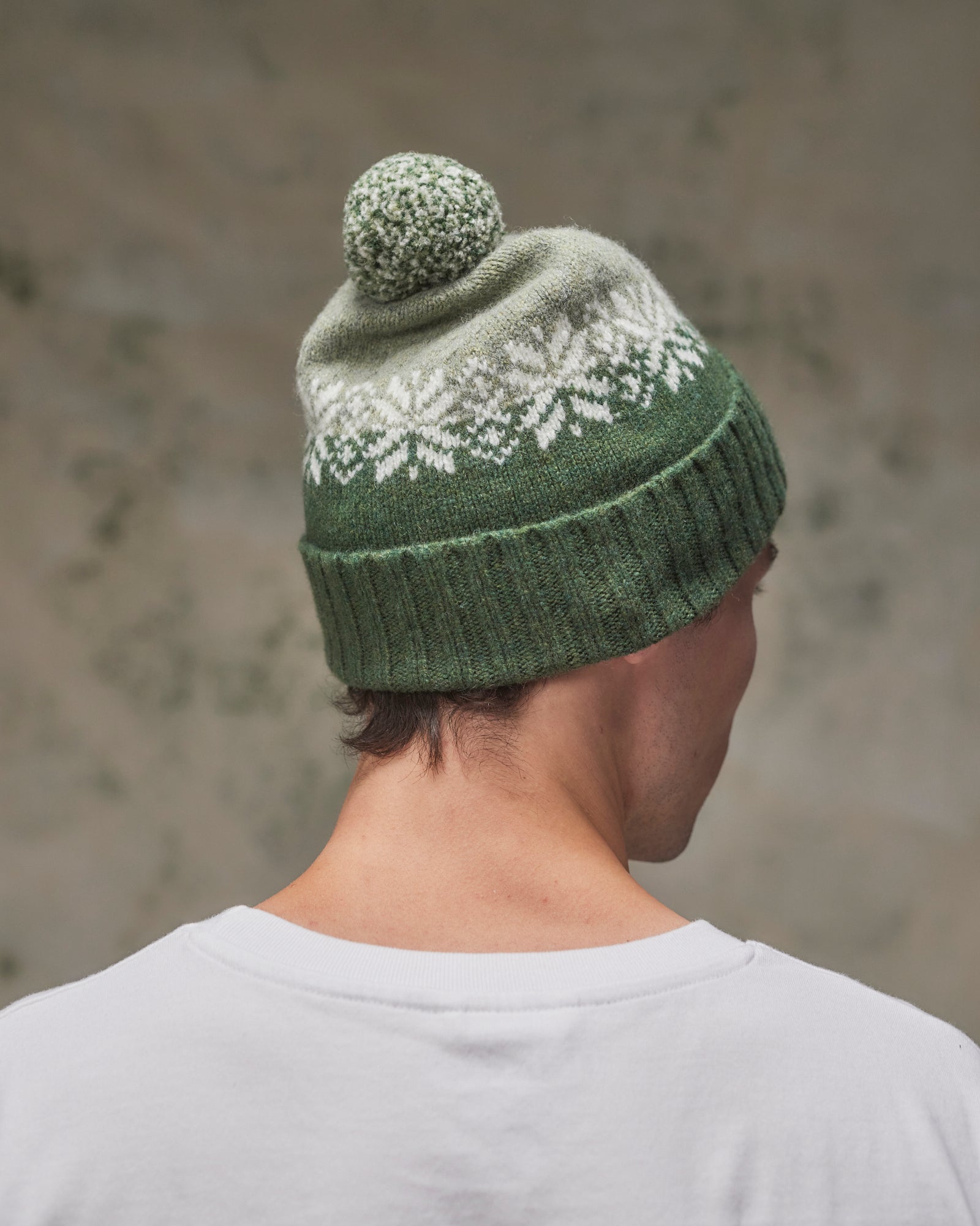 Back view of model wearing the coriander Fair Isle pattern hat from Uskees, clearly showing the tricolour design, snowflakes and bobble.