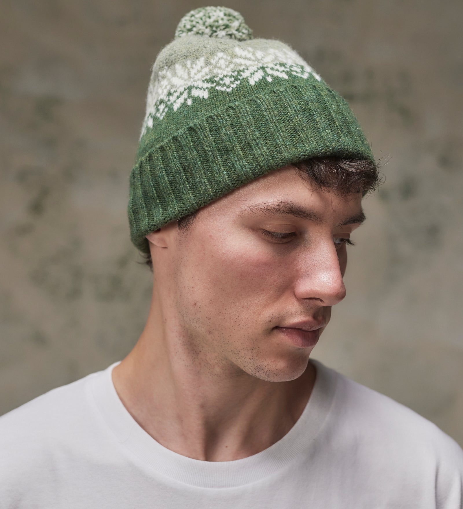 Side view of model wearing the coriander Fair Isle pattern hat from Uskees, clearly showing the tricolour design, snowflakes and bobble.