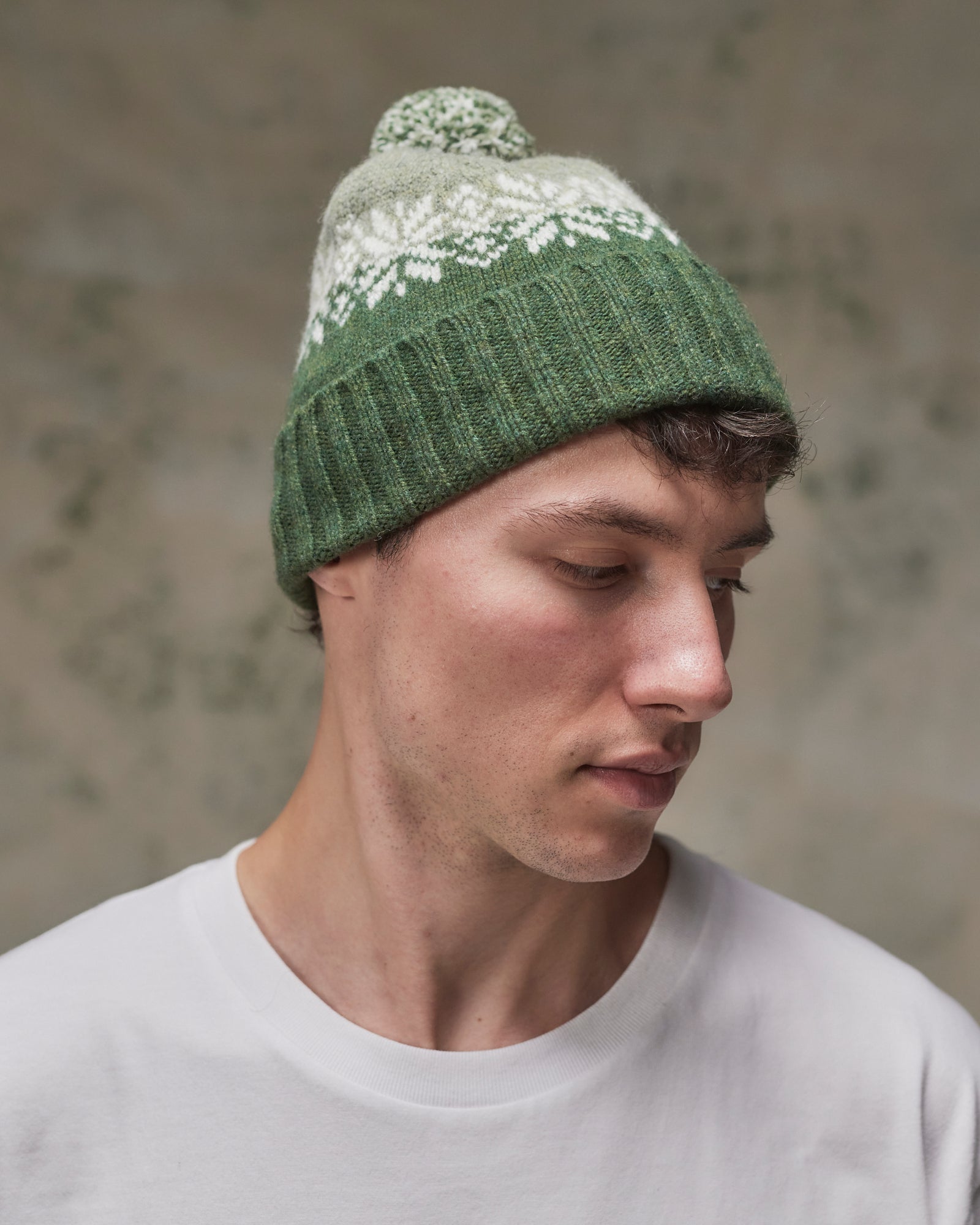 Side view of model wearing the coriander Fair Isle pattern hat from Uskees, clearly showing the tricolour design, snowflakes and bobble.
