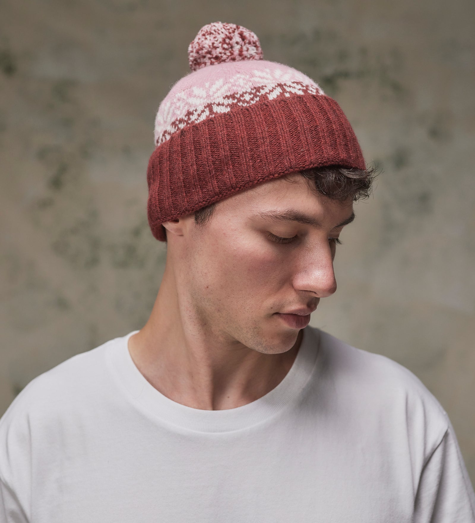 Side view of model wearing the dusty pink Fair Isle pattern hat from Uskees, clearly showing the tricolour design, snowflakes and bobble.