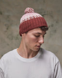 Side view of model wearing the dusty pink Fair Isle pattern hat from Uskees, clearly showing the tricolour design, snowflakes and bobble.