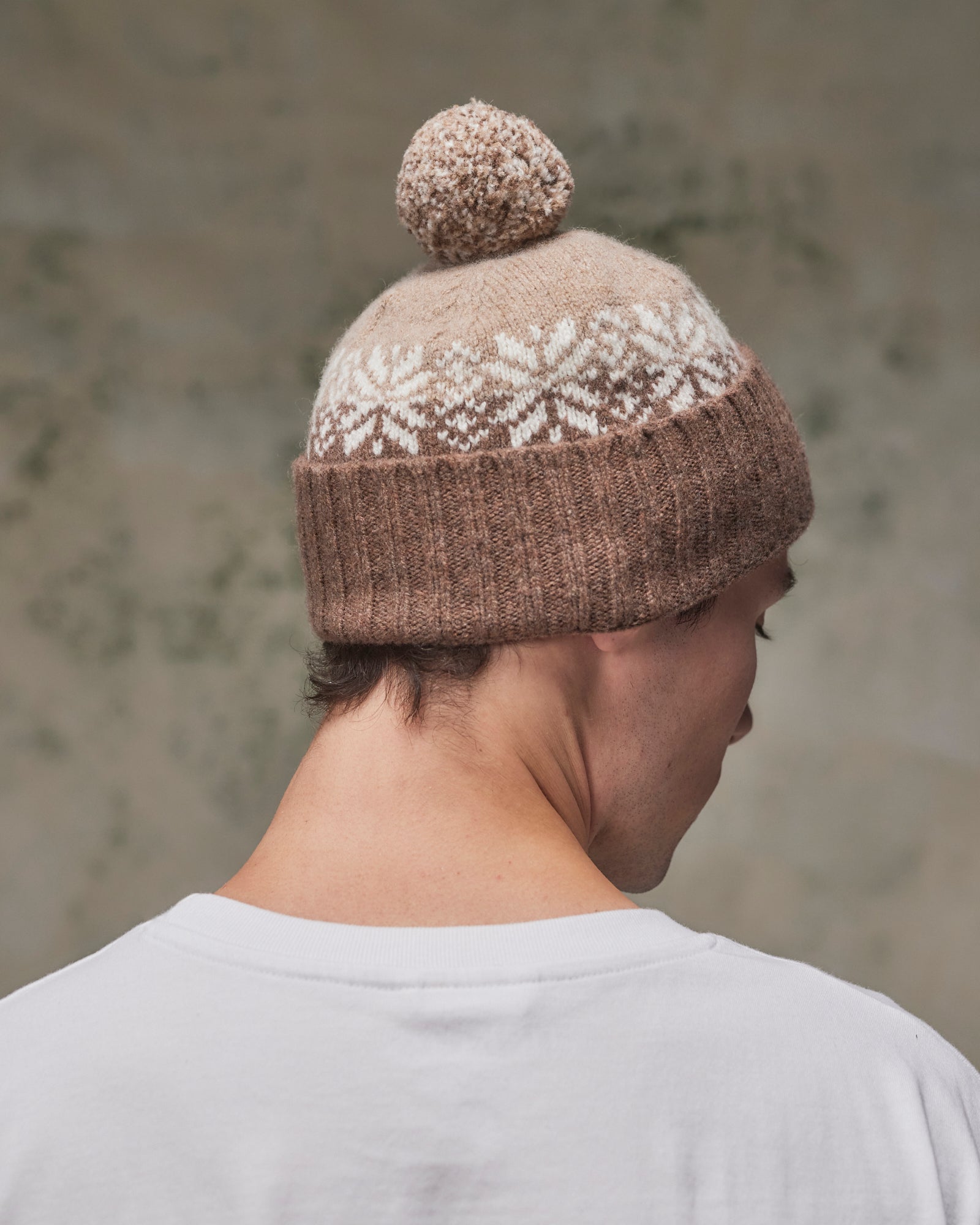 Back view of model wearing the khaki Fair Isle pattern hat from Uskees, clearly showing the tricolour design, snowflakes and bobble.