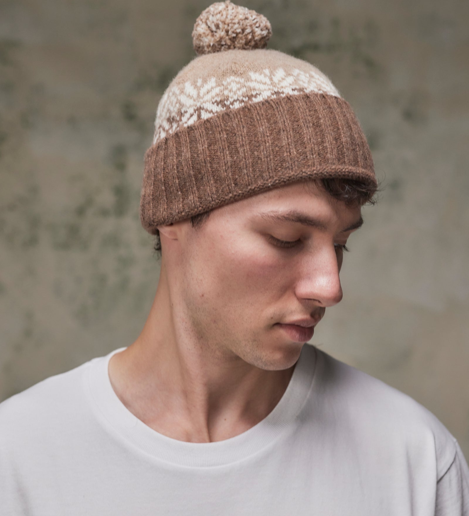 Side view of model wearing the khaki Fair Isle pattern hat from Uskees, clearly showing the tricolour design, snowflakes and bobble.