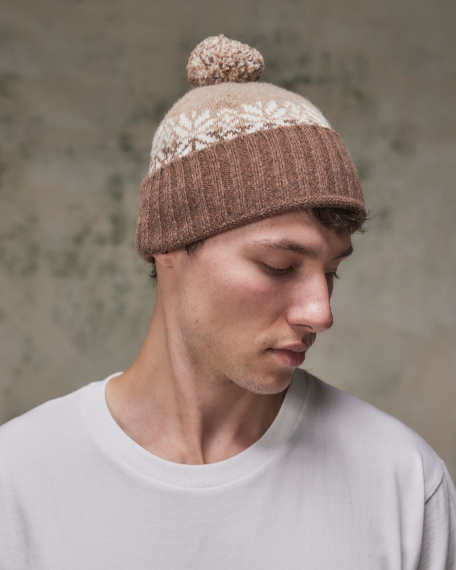 Side view of model wearing the khaki Fair Isle pattern hat from Uskees, clearly showing the tricolour design, snowflakes and bobble.