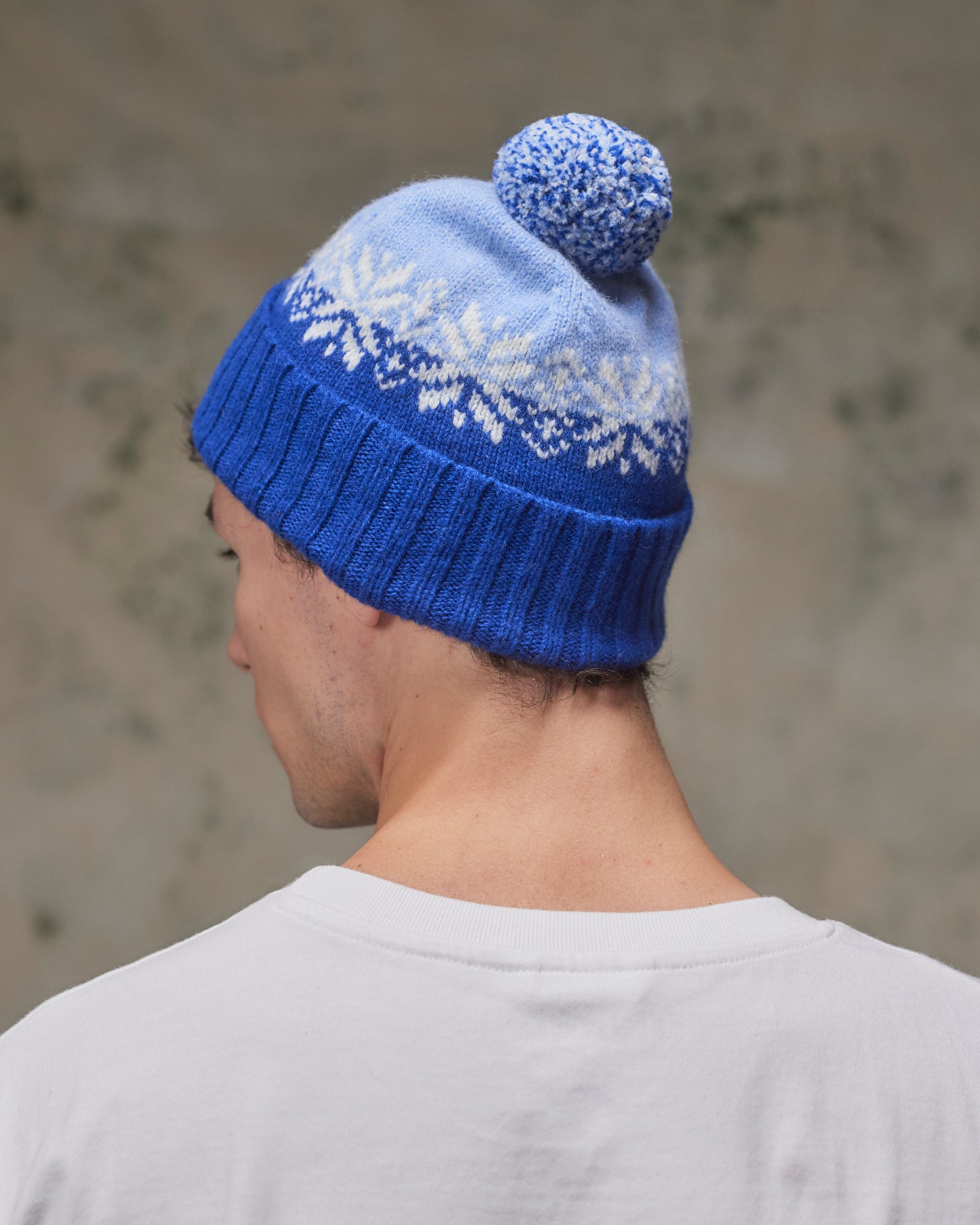 Back view of model wearing the ultra blue Fair Isle pattern hat from Uskees, clearly showing the tricolour design, snowflakes and bobble.