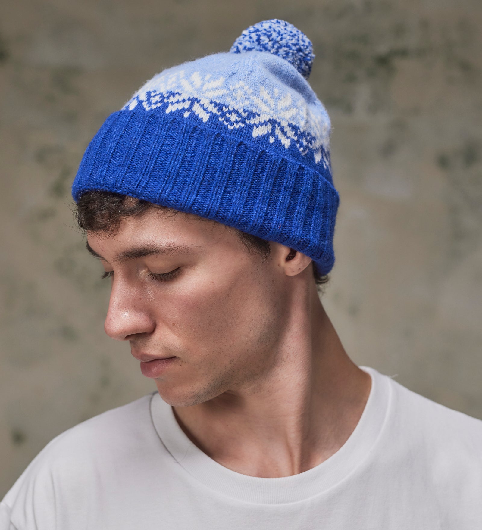 Side view of model wearing the ultra blue Fair Isle pattern hat from Uskees, clearly showing the tricolour design, snowflakes and bobble.