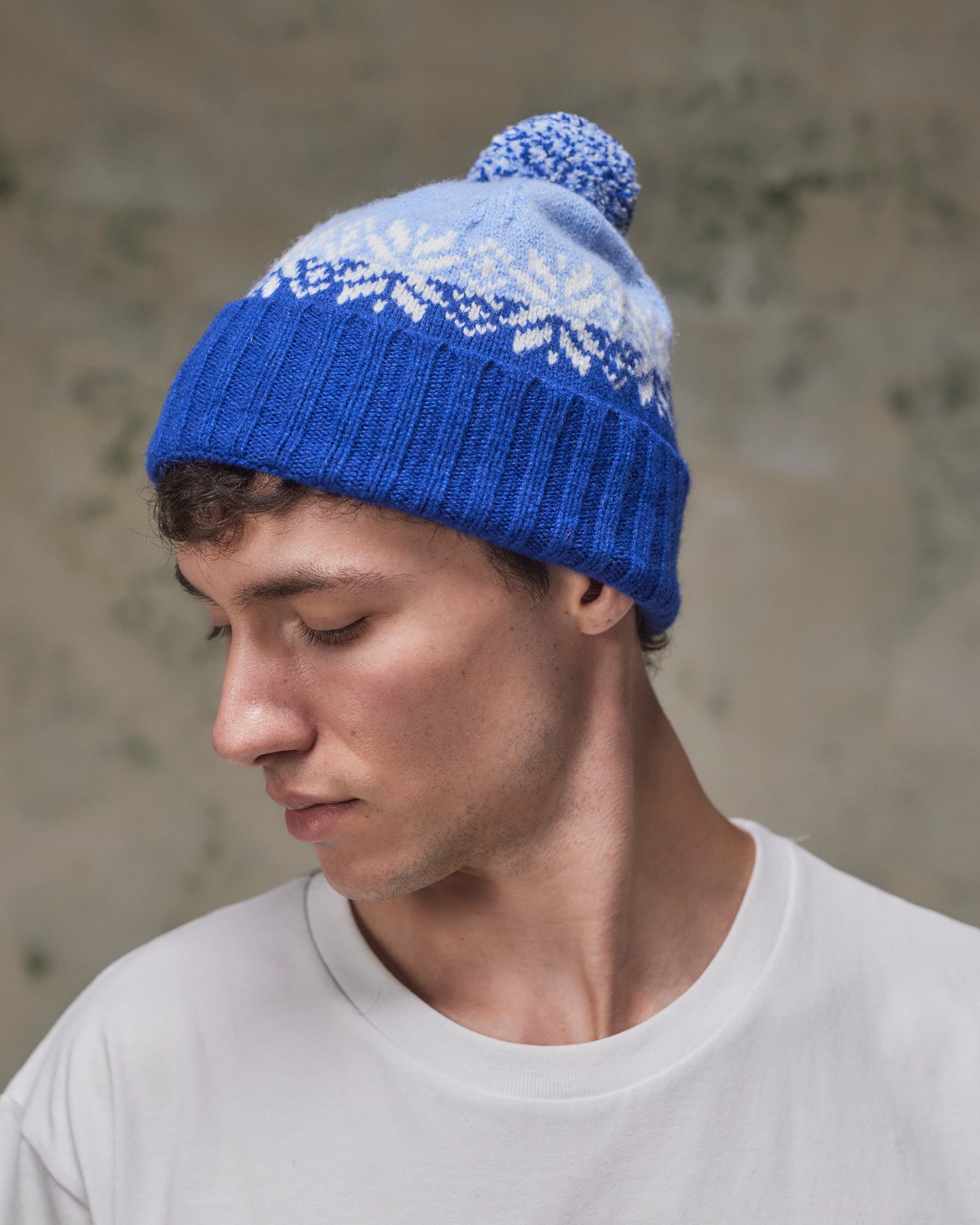 Side view of model wearing the ultra blue Fair Isle pattern hat from Uskees, clearly showing the tricolour design, snowflakes and bobble.