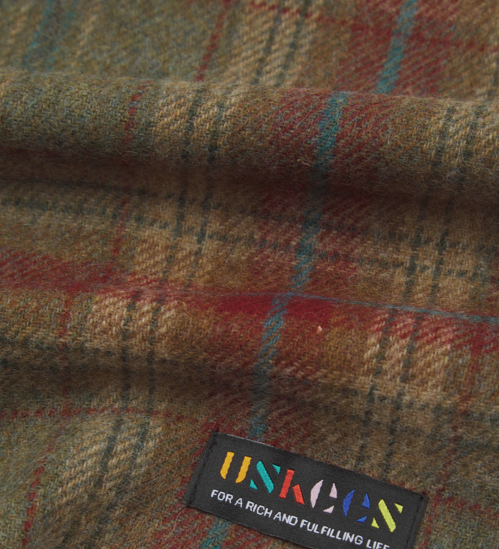 Close up view of Uskees tartan lambswool scarf showing the green and red pattern and uskees brand label.