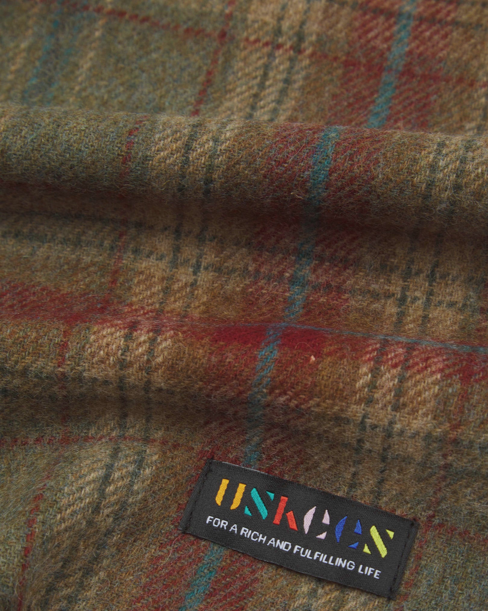 Close up view of Uskees tartan lambswool scarf showing the green and red pattern and uskees brand label.