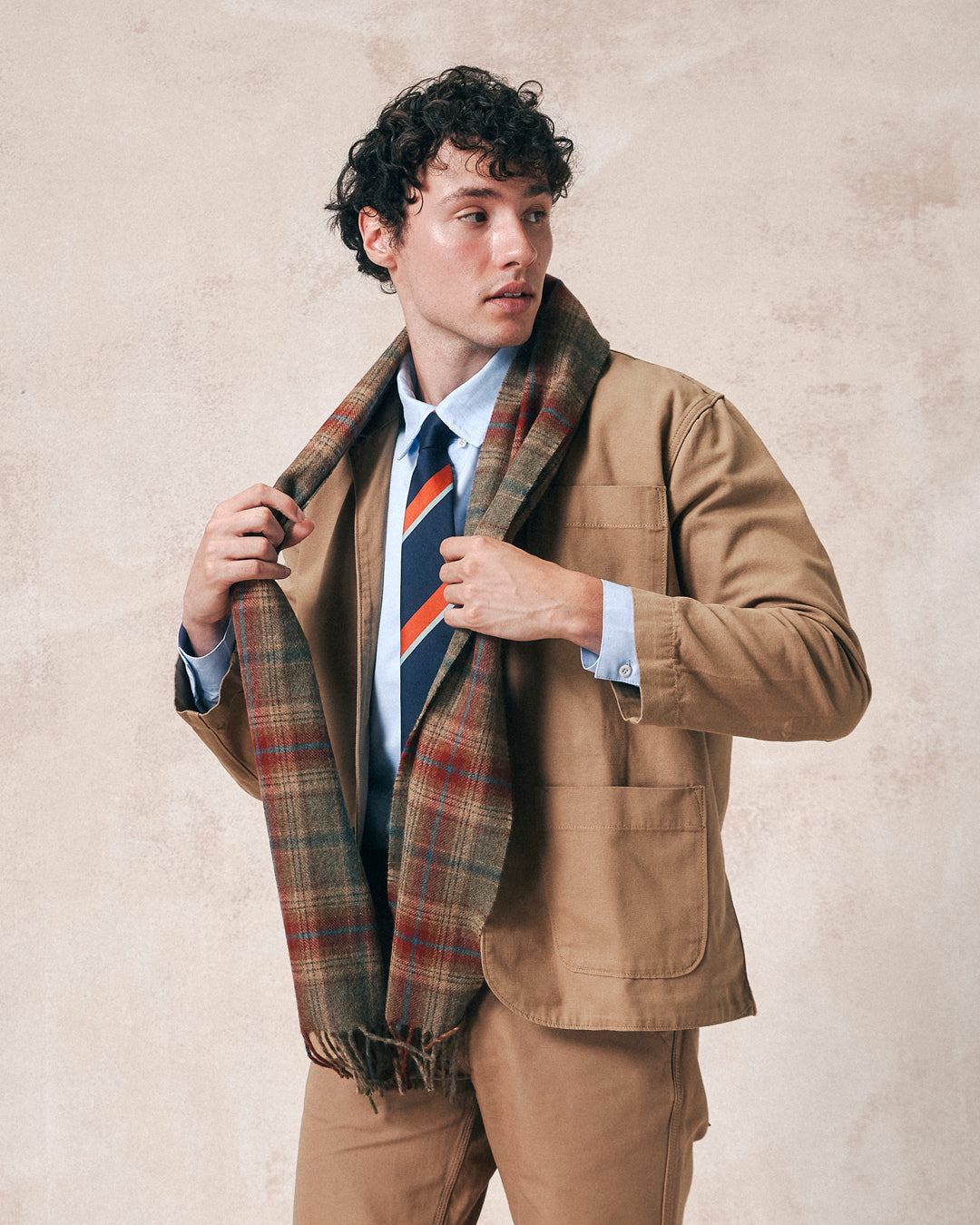 Two-thirds angled view of model wearing 4013 clay tartan scarf from Uskees. Paired with khaki-coloured Uskees suit and tricolour tie.