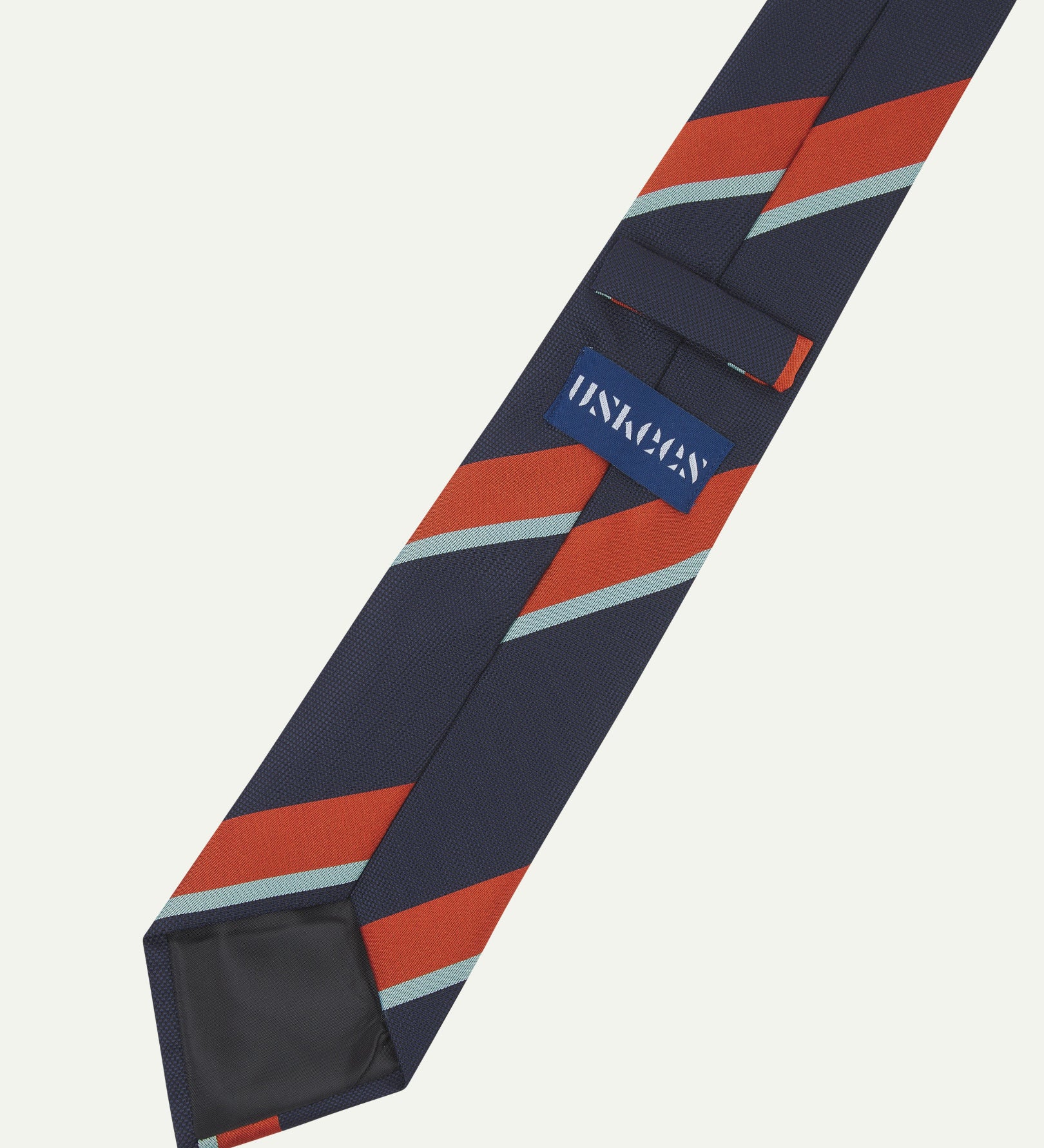 Close-up reverse view of recycled polyester repp tie, showing tricolour stripes, Uskees branding label, tie loop and black lining.