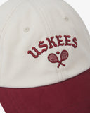 Close-up front view of cream and maroon Uskees cap with 'USKEES' and tennis racquet motif embroidered in maroon.