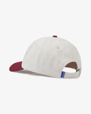 Side view of an Uskees cream and maroon baseball cap showing the panels, the adjustable strap with metal fastener and a blue 'USKEES' logo tab.