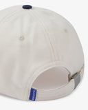 Close-up back view of cream and navy blue Uskees cap with focus on the cord material, vents, adjustable strap with metal fastener and 'USKEES' logo tab.