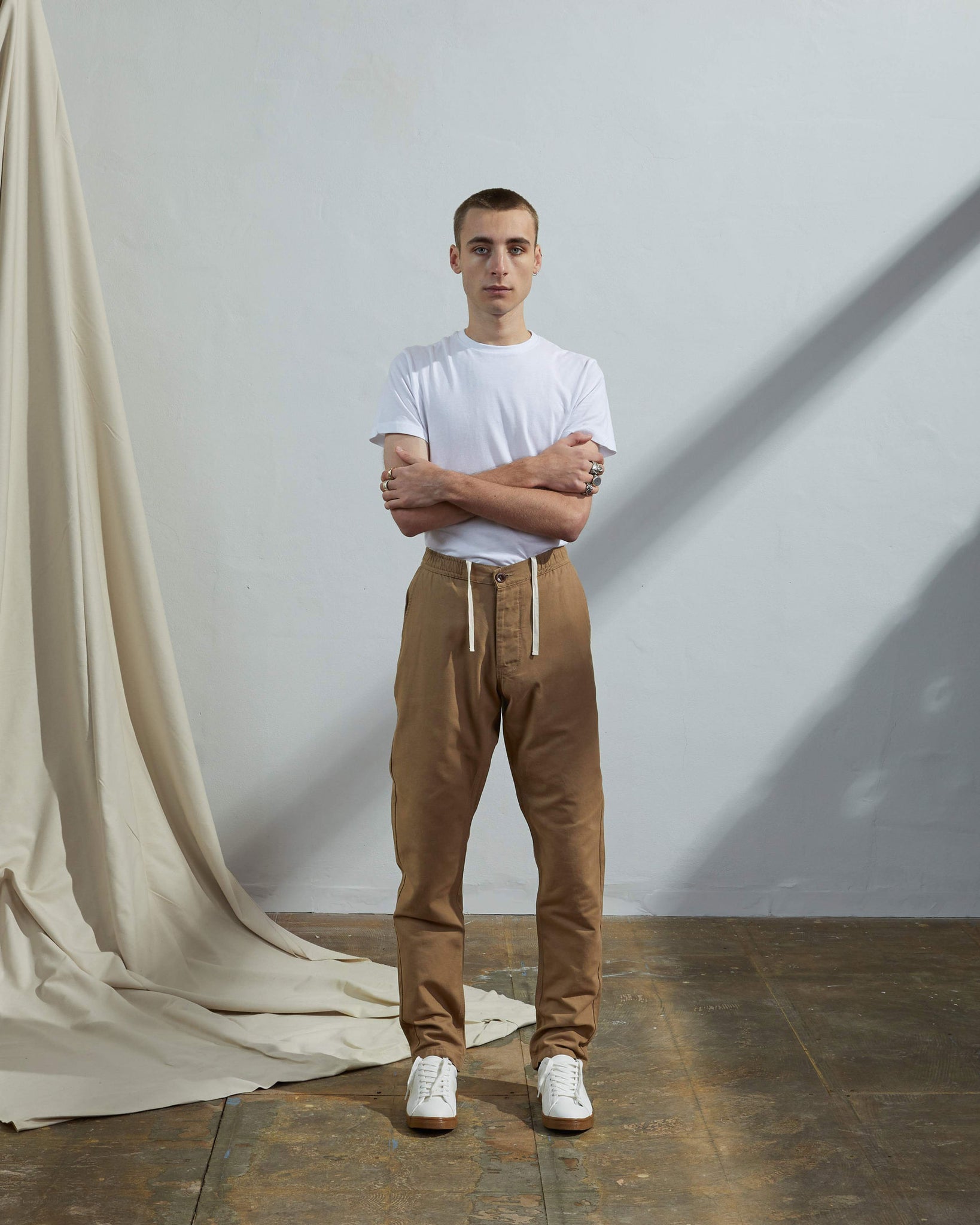 Full-length, front view of model wearing Uskees men's organic cotton 'khaki' casual drawstring pants. Paired with white t-shirt.