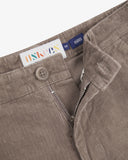 Close-up view of Uskees brown corduroy pants for men showing the brand label and fly zip (half open) and button detail.